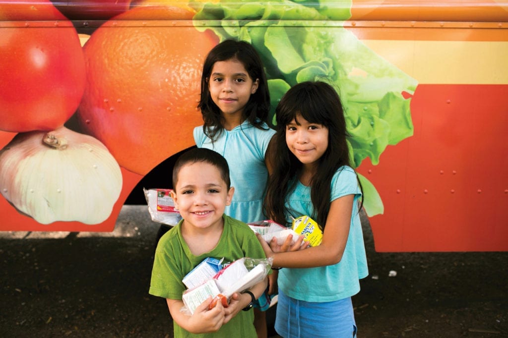 Children standing in front of a bus holding food supplied by No Kid Hungry